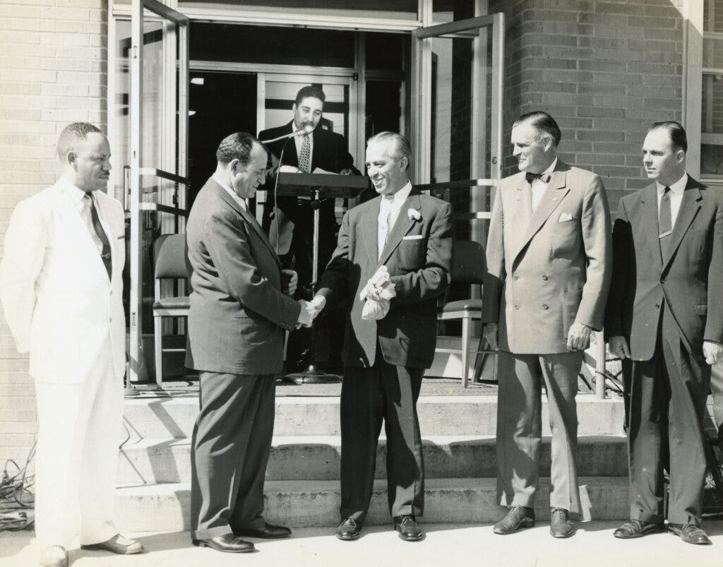 A group of men in suits with Dr. Harry Penn shaking a man's hand