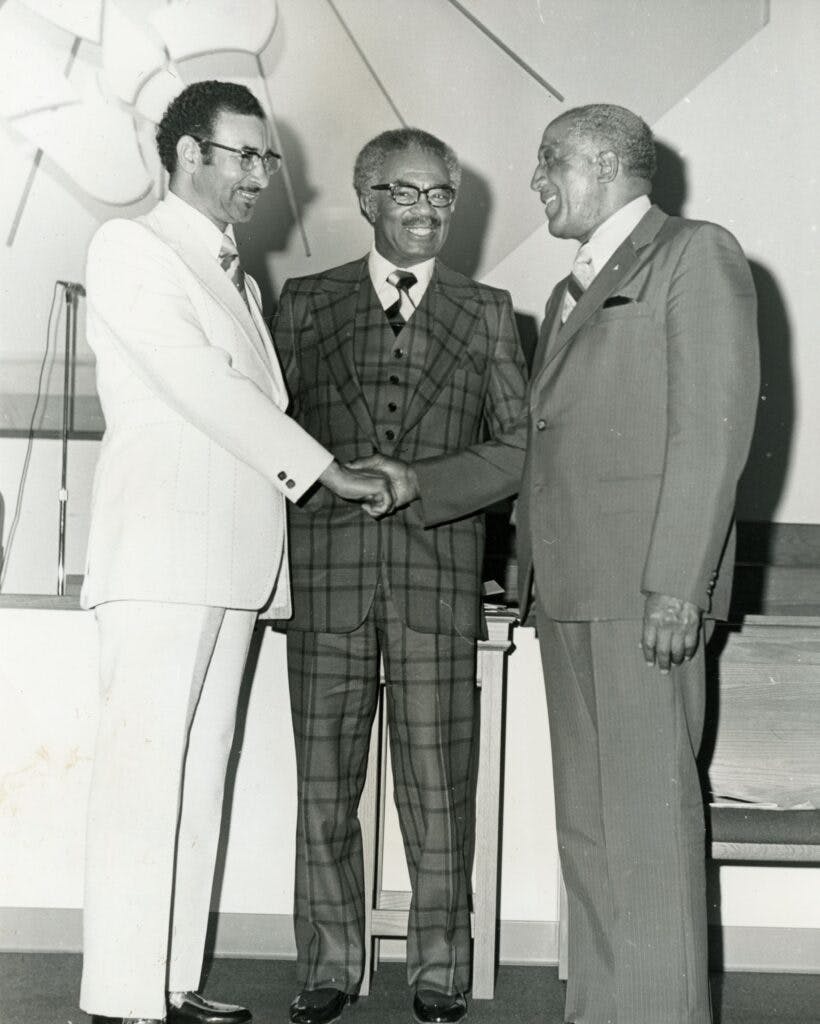 A black and white photo of an unidentified man, Dr. Law and Rev. Noel C. Taylor all in suits, smiling.