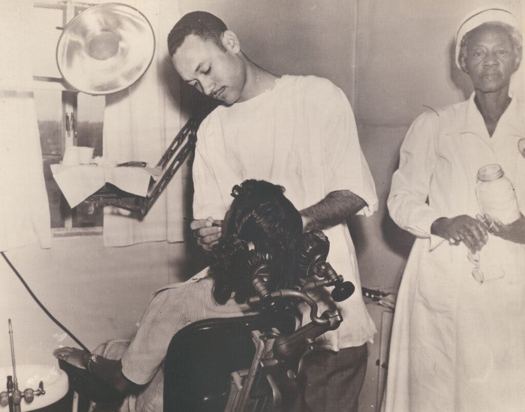 A woman getting dental work done with nurse Daisy Schley in the background looking at the camera