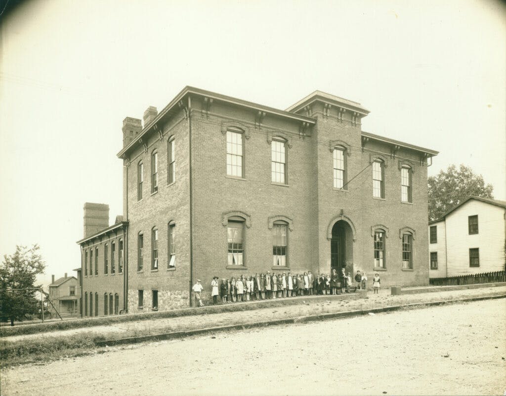 Photo of the two main story building with students lined up out front