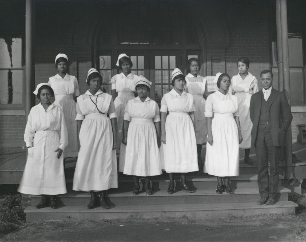A group of nurses in their white dress uniforms and hats, with Dr. Roberts standing next to them in a suit.