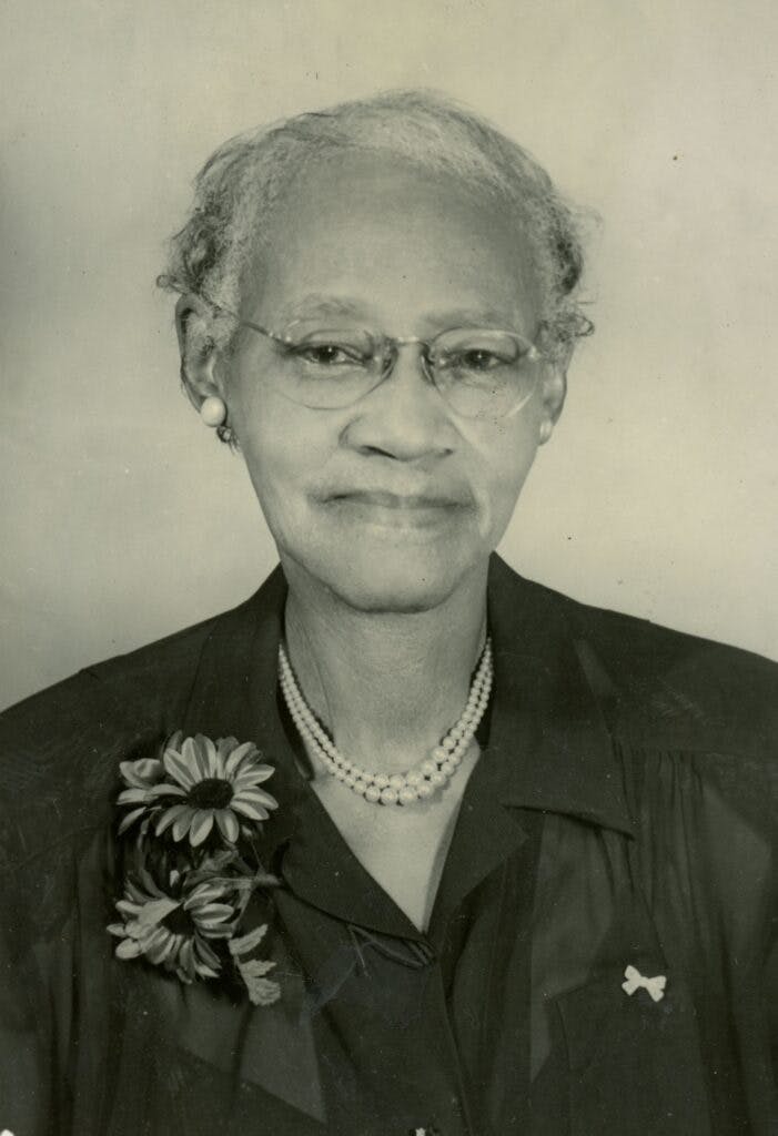 A portrait of Daisy Schley with flowers on her lapel and a pearl necklace