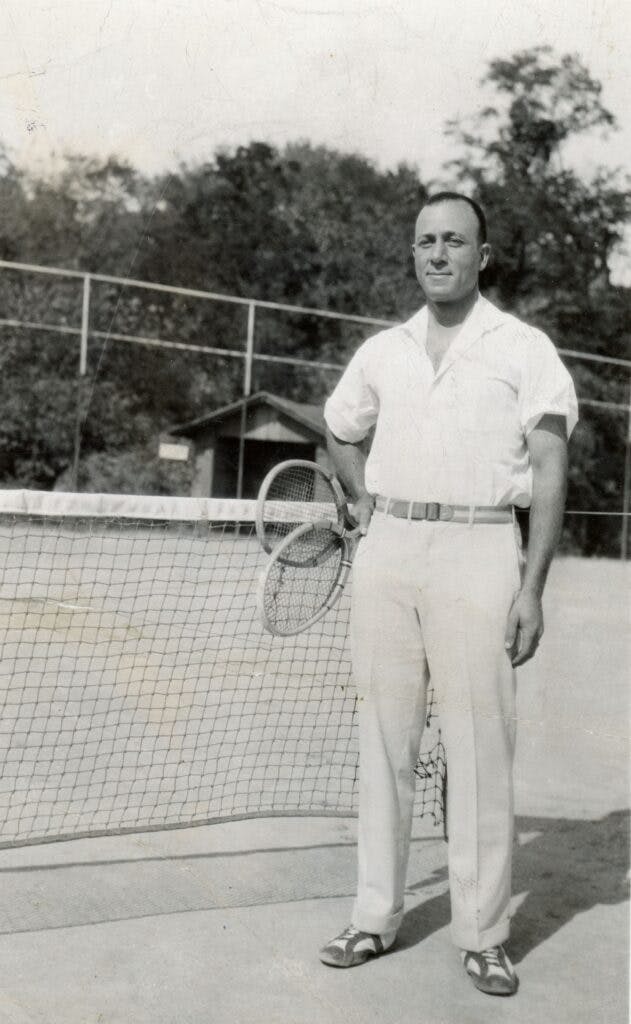 Dr. Downing proudly standing on a tennis court with two tennis rackets in hand