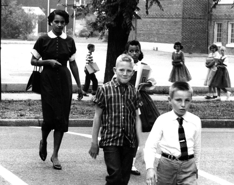 Two white boys smirk at the camera while Mrs. George Long escorts her daughter Sheryl, with markedly different expressions from the two boys in front of them. Sheryl has a straight face, glancing off to her right, while her mother flatly looks straight ahead.