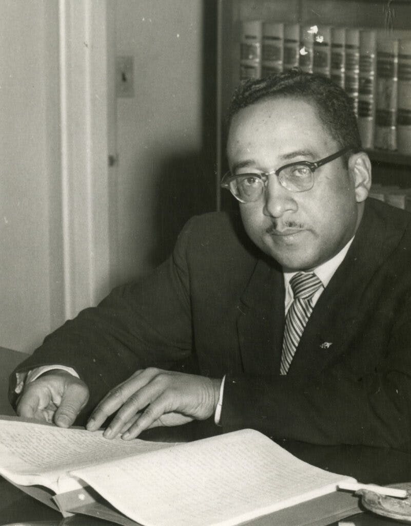 Photo of Reuben Lawson, likely in his office, looking over papers with books behind him